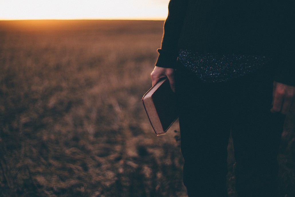 Believer holding an open Bible in a field at sunset